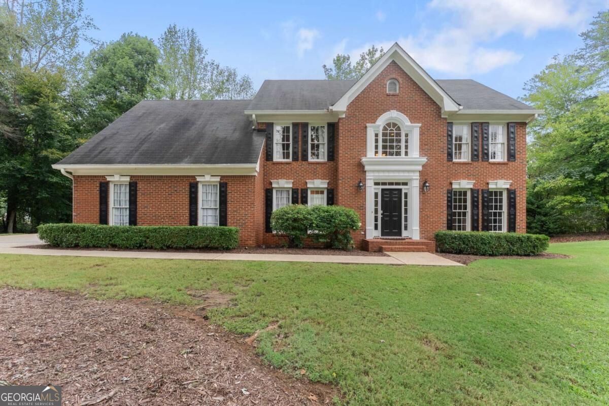 Two-story red-brick house with black shutters and a broad front lawn.