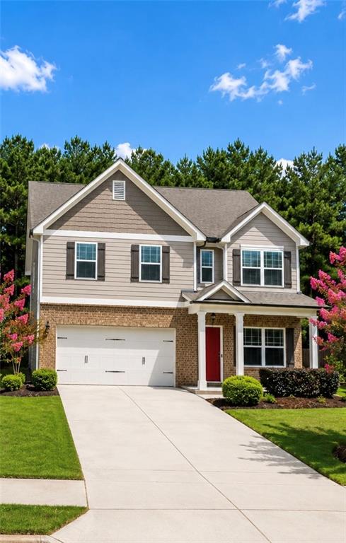 Two-story beige and brick house with a red front door, double garage, and flowering trees.