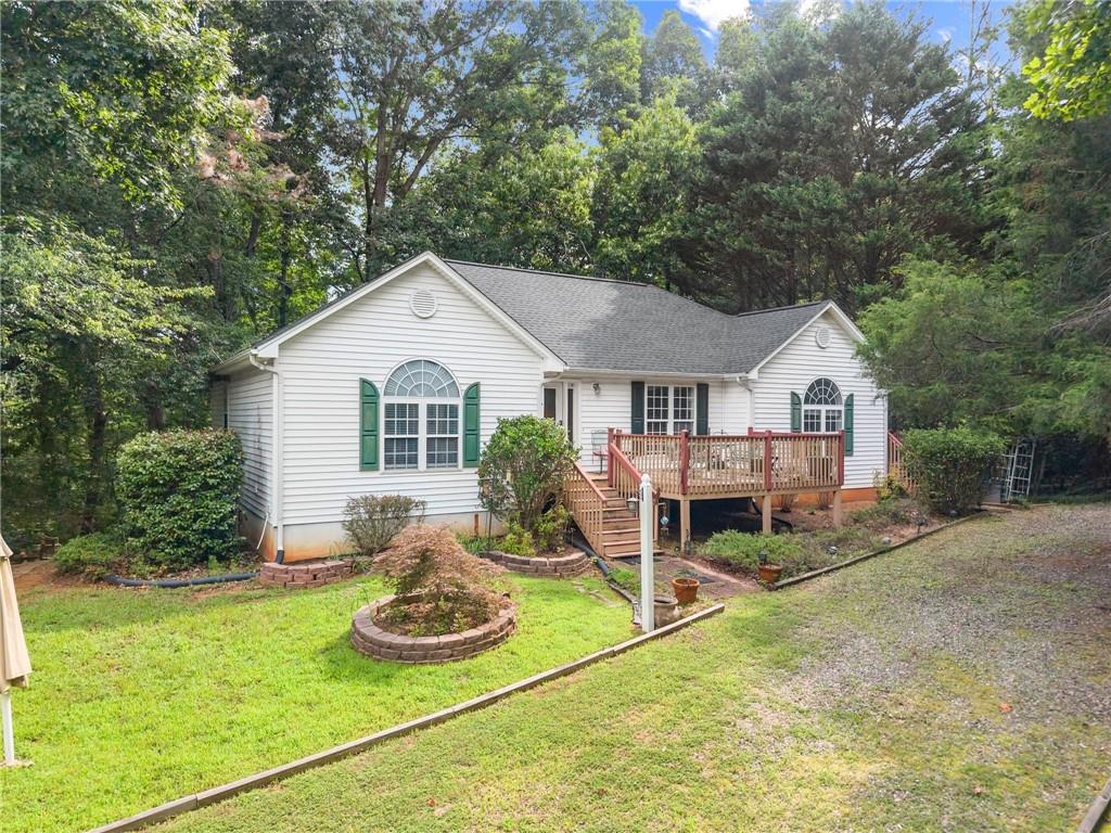 White house with green shutters and a raised wooden deck, surrounded by mature trees.