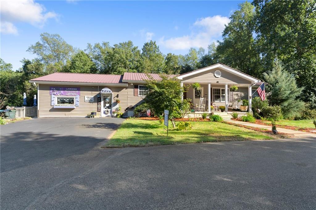Tan flower shop with a red metal roof, covered porch, landscaped lawn, and American flag.