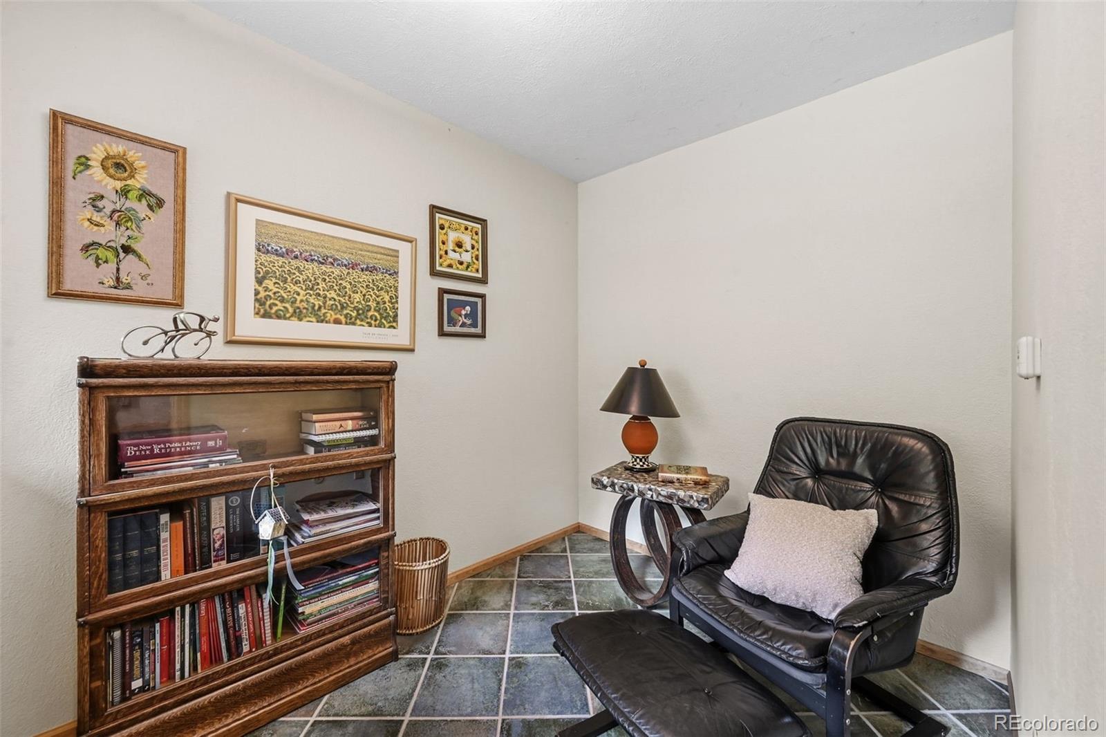 Furnished study with a black leather lounge chair, ottoman, and book-filled wooden bookcase.
