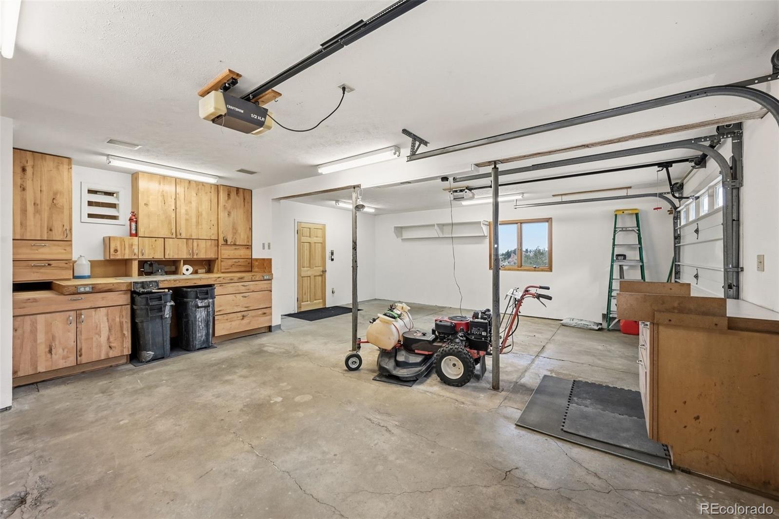 Spacious garage with wooden workshop cabinetry, a concrete floor, and lawn equipment.