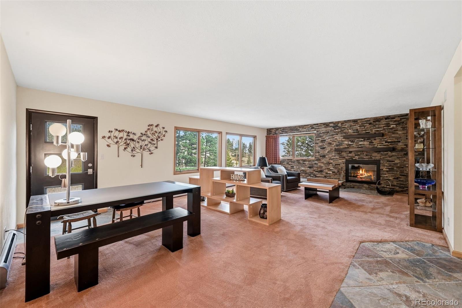 Furnished living room with a stone fireplace wall, large windows, and a table in the foreground.