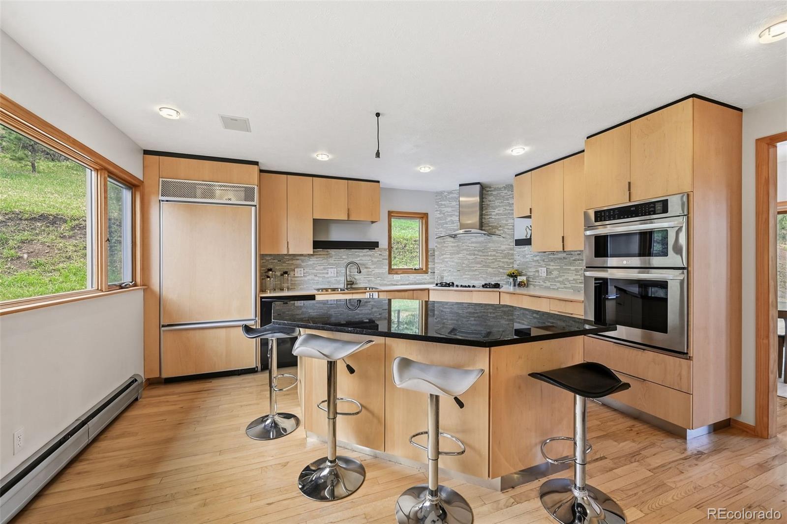 Kitchen with a black island, three bar stools, light wood cabinets, and stainless steel appliances.