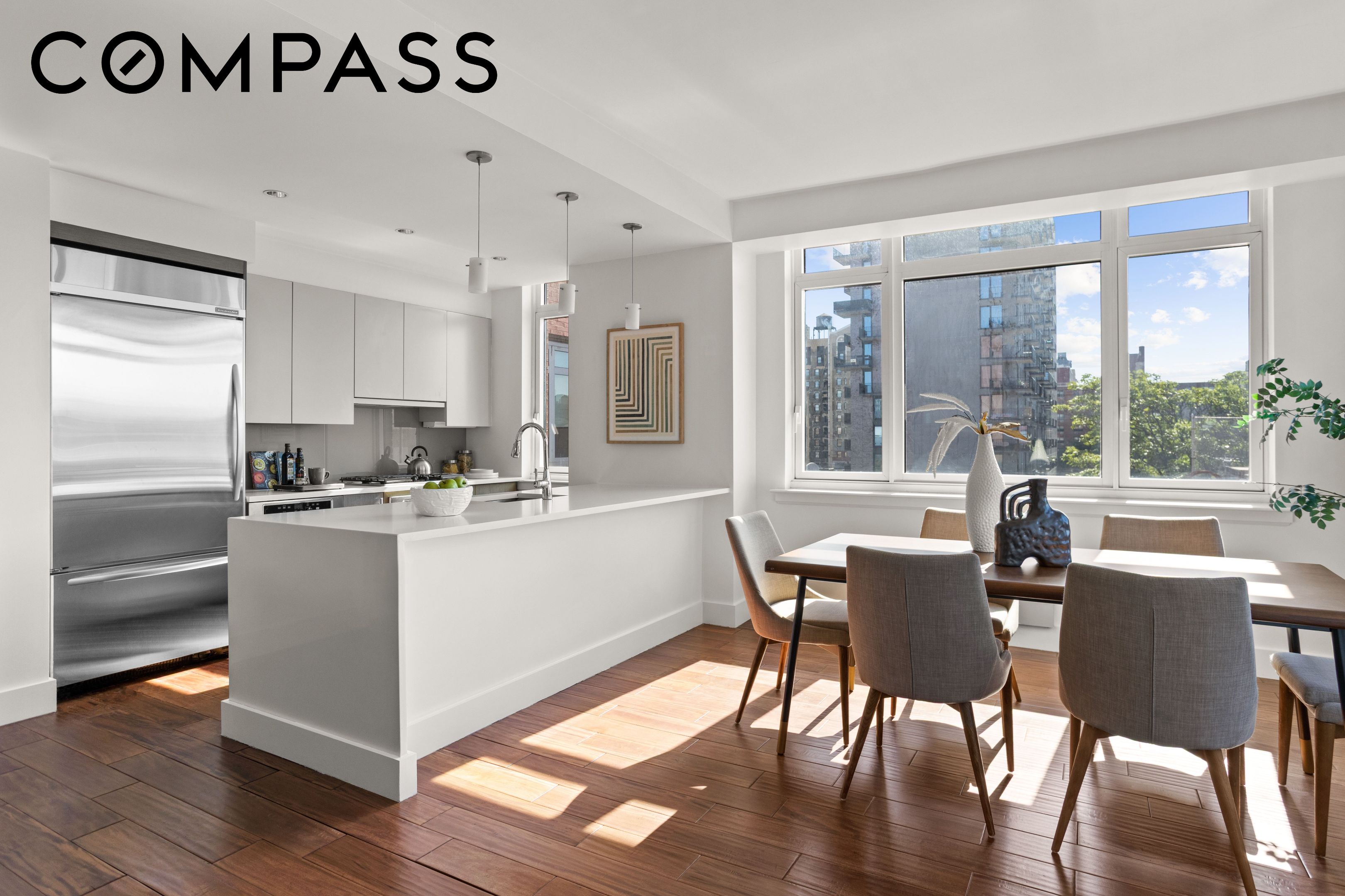 Bright open-plan kitchen and dining area with large windows, city views, and hardwood floors.