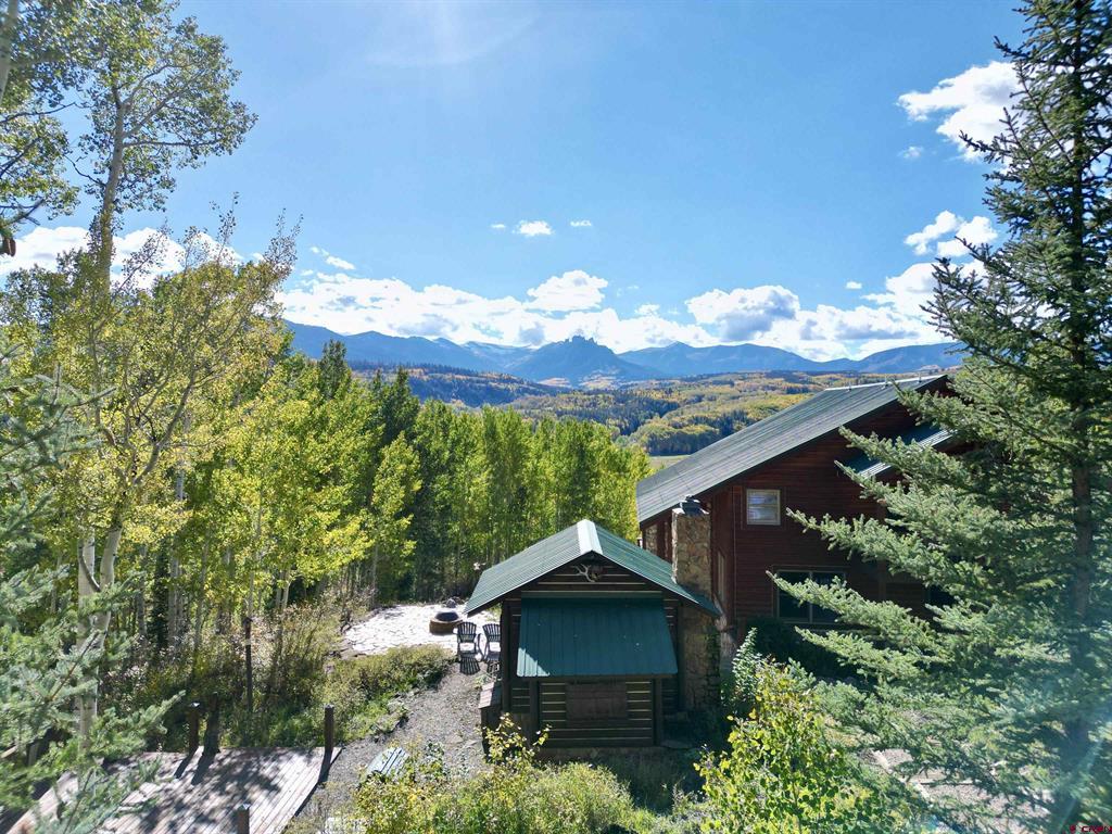 Mountain home overlooking an autumn valley, with evergreens and a broad mountain range.