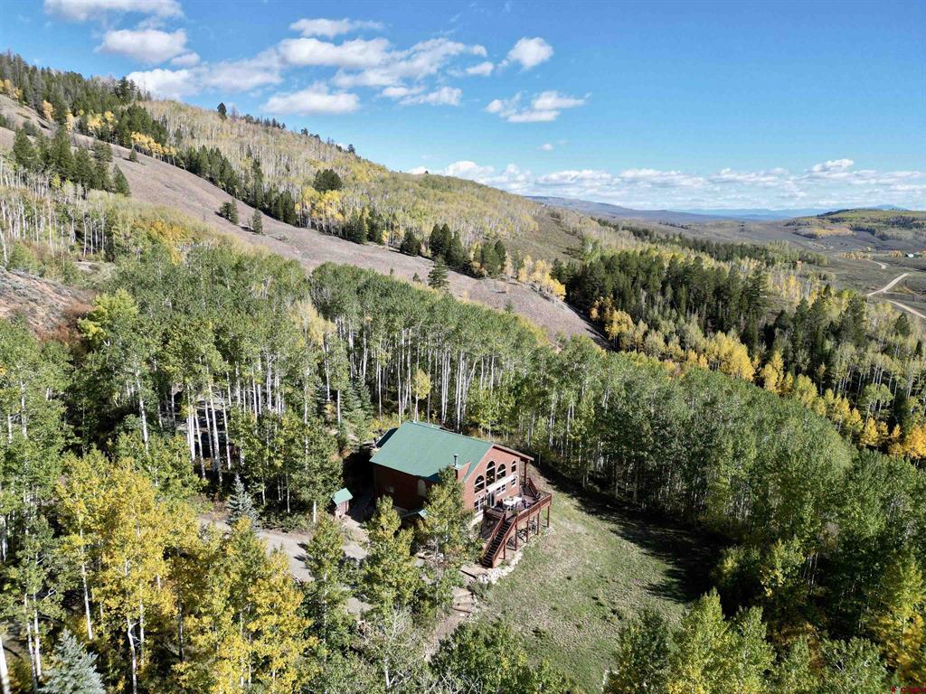 Aerial view of a green-roofed mountain home among autumn aspens, evergreens, and rolling hills.