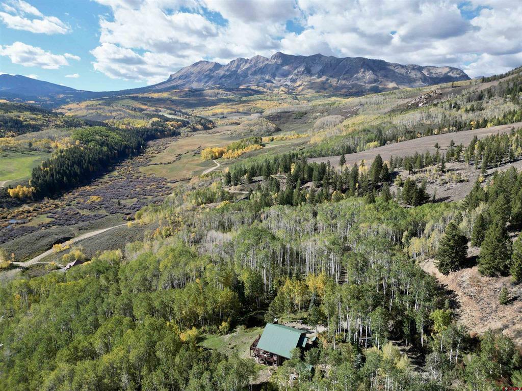 Aerial view of a mountain valley with autumn trees and a cabin in the foreground.