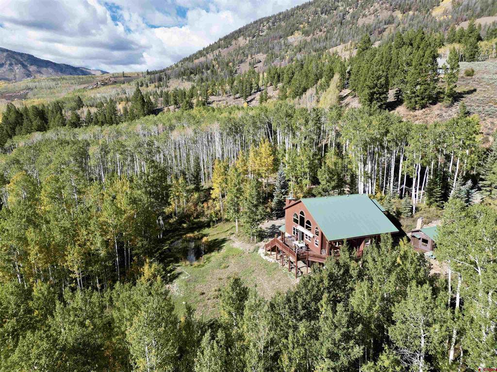 Mountain home with a green roof and deck, surrounded by autumn forest and mountain slopes.