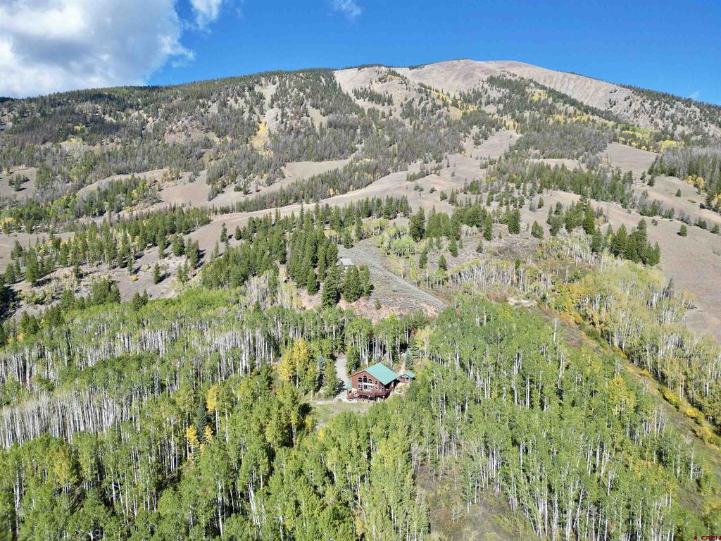 Aerial view of a secluded cabin among autumn aspens, with open mountain slopes beyond.