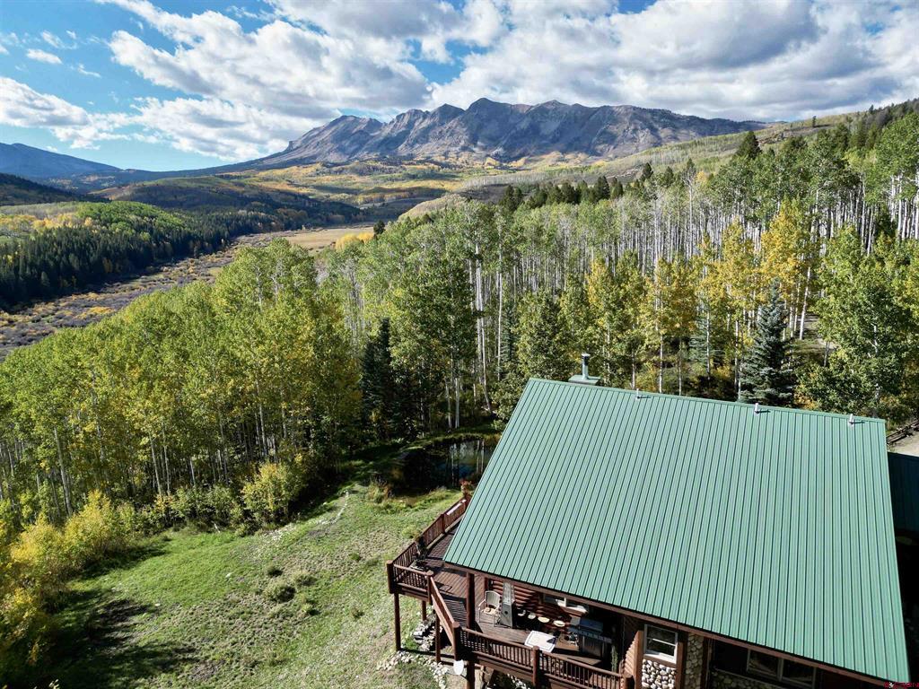 Aerial view of a mountain home with a green metal roof, deck, and autumn aspens.