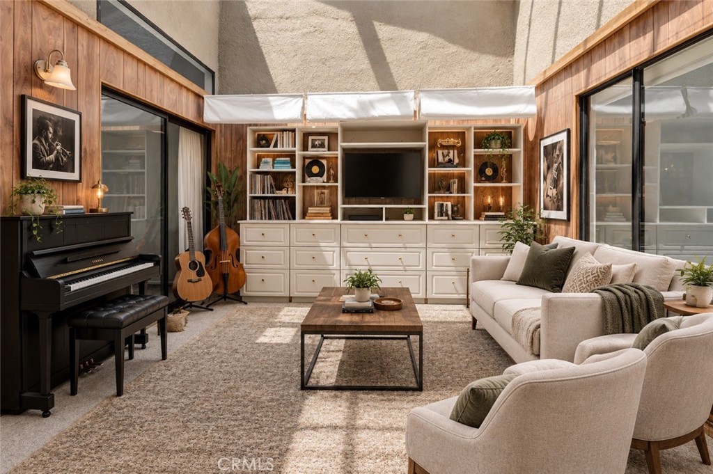 Living room with built-in shelving, a piano, guitars, and a vaulted ceiling.