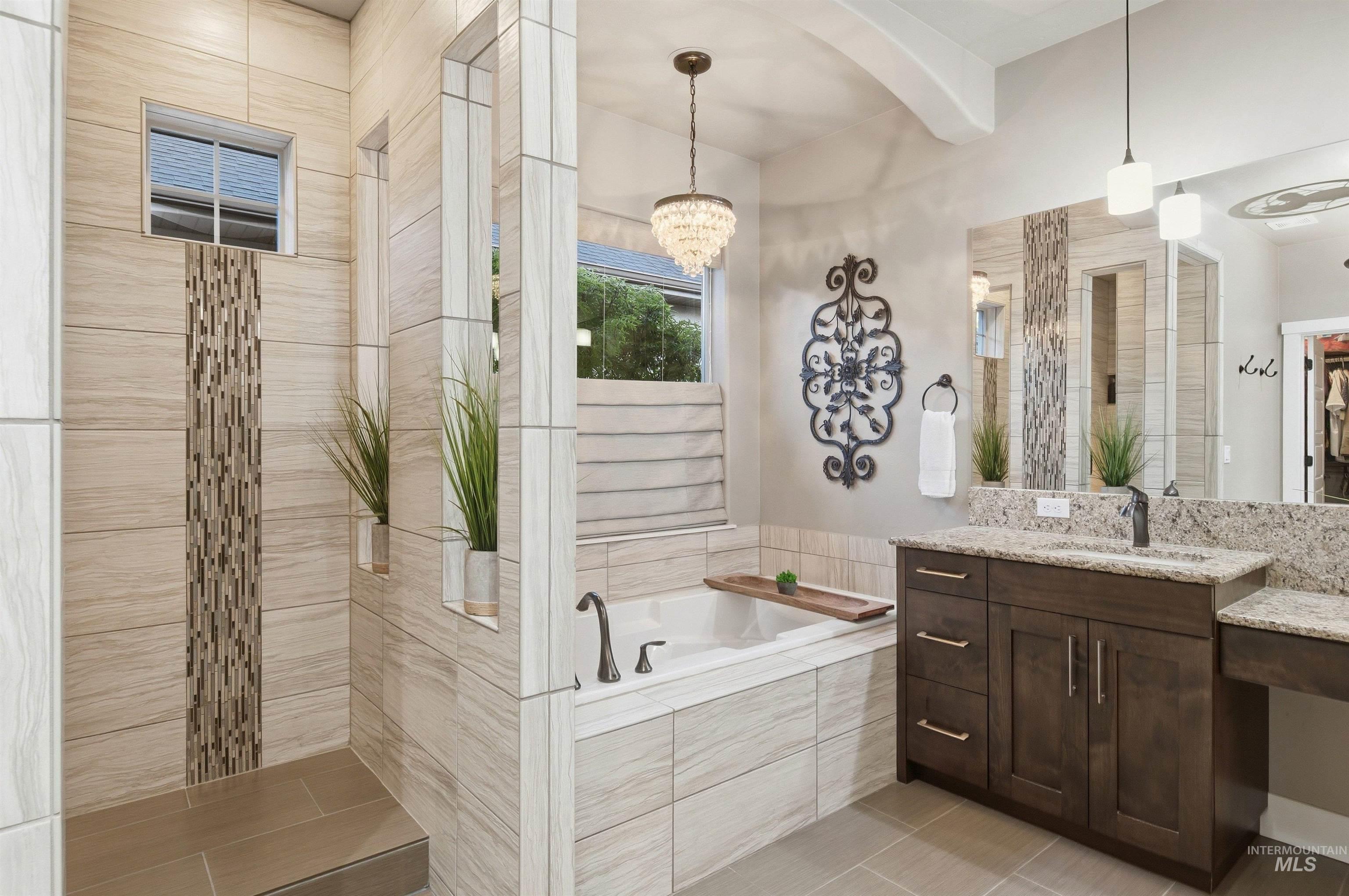 Primary bathroom with a tiled soaking tub, dark wood vanity, and chandelier.
