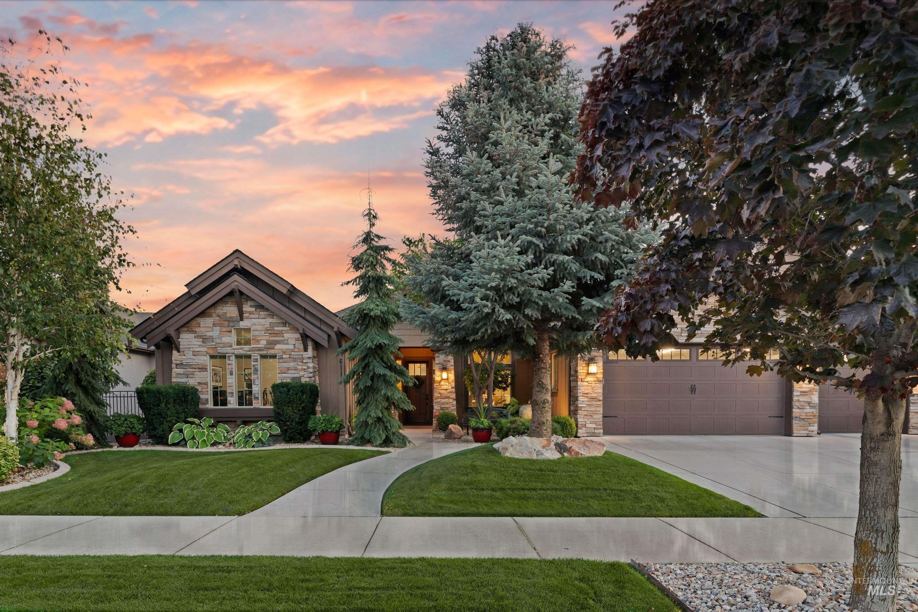 Stone-front home with an attached garage, curved walkway, and mature trees at sunset.
