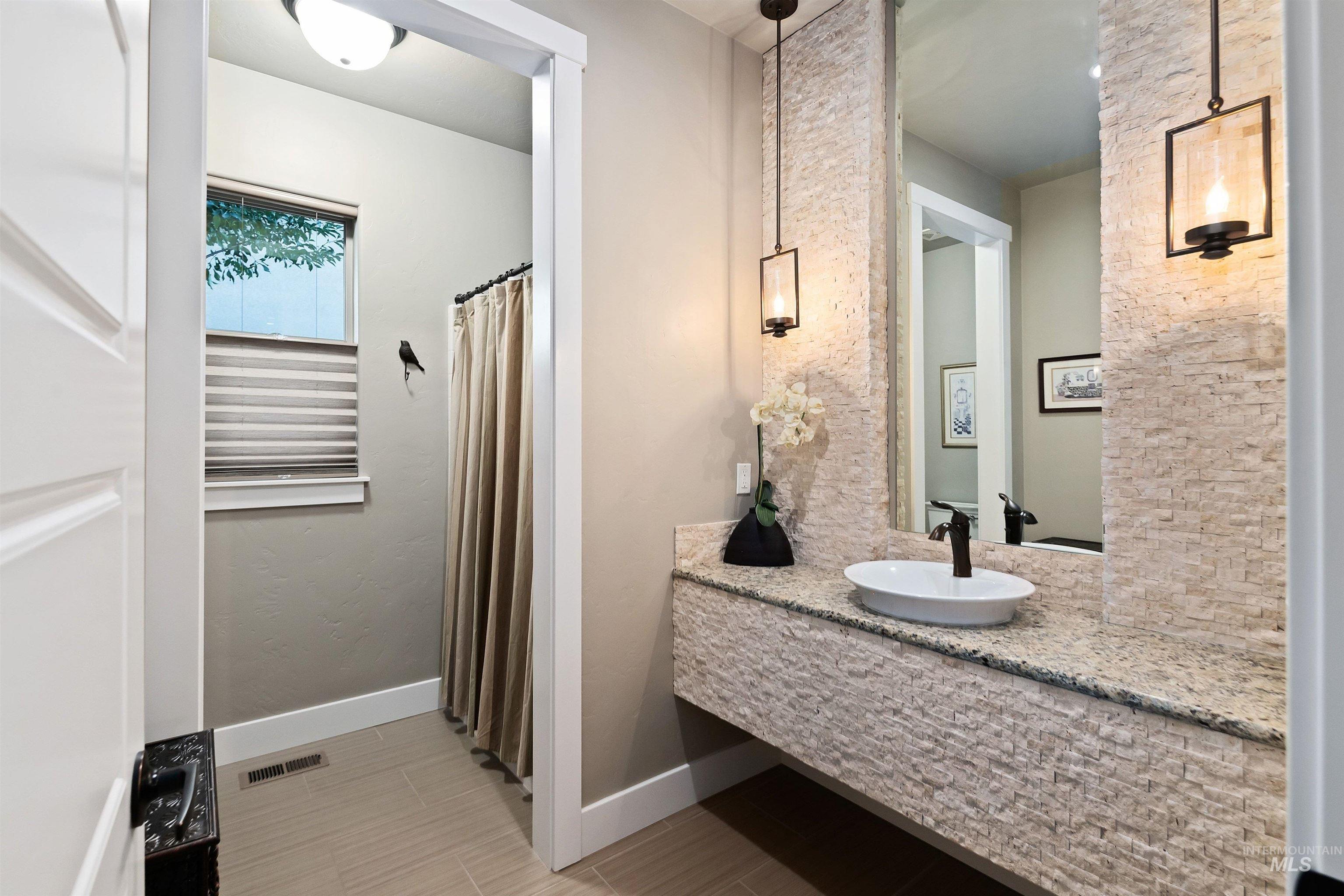 Bathroom with a stone-tiled floating vanity, vessel sink, and shower beside a window.