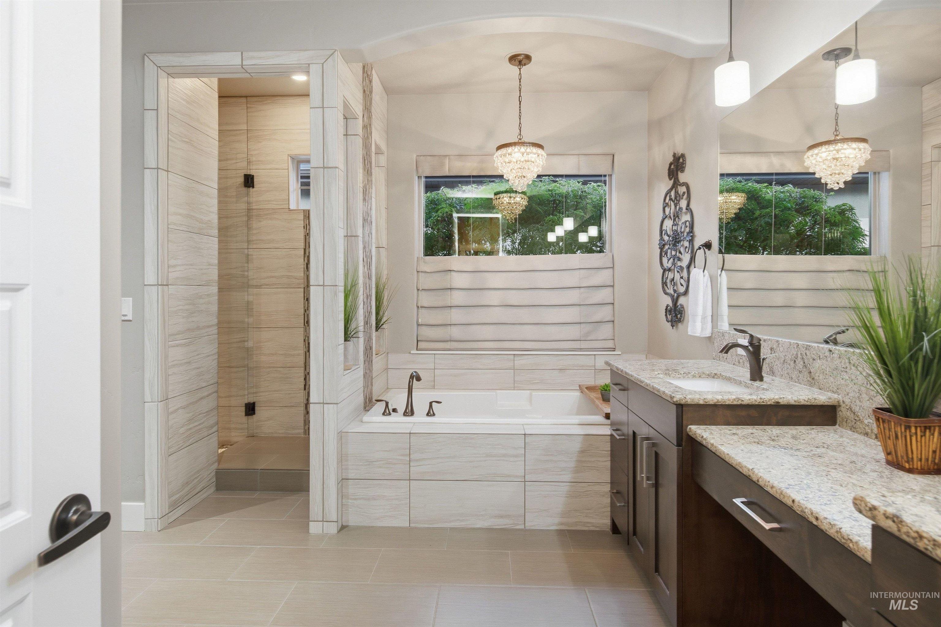 Bathroom with a glass shower, soaking tub beneath a wide window, and granite-topped double vanity.