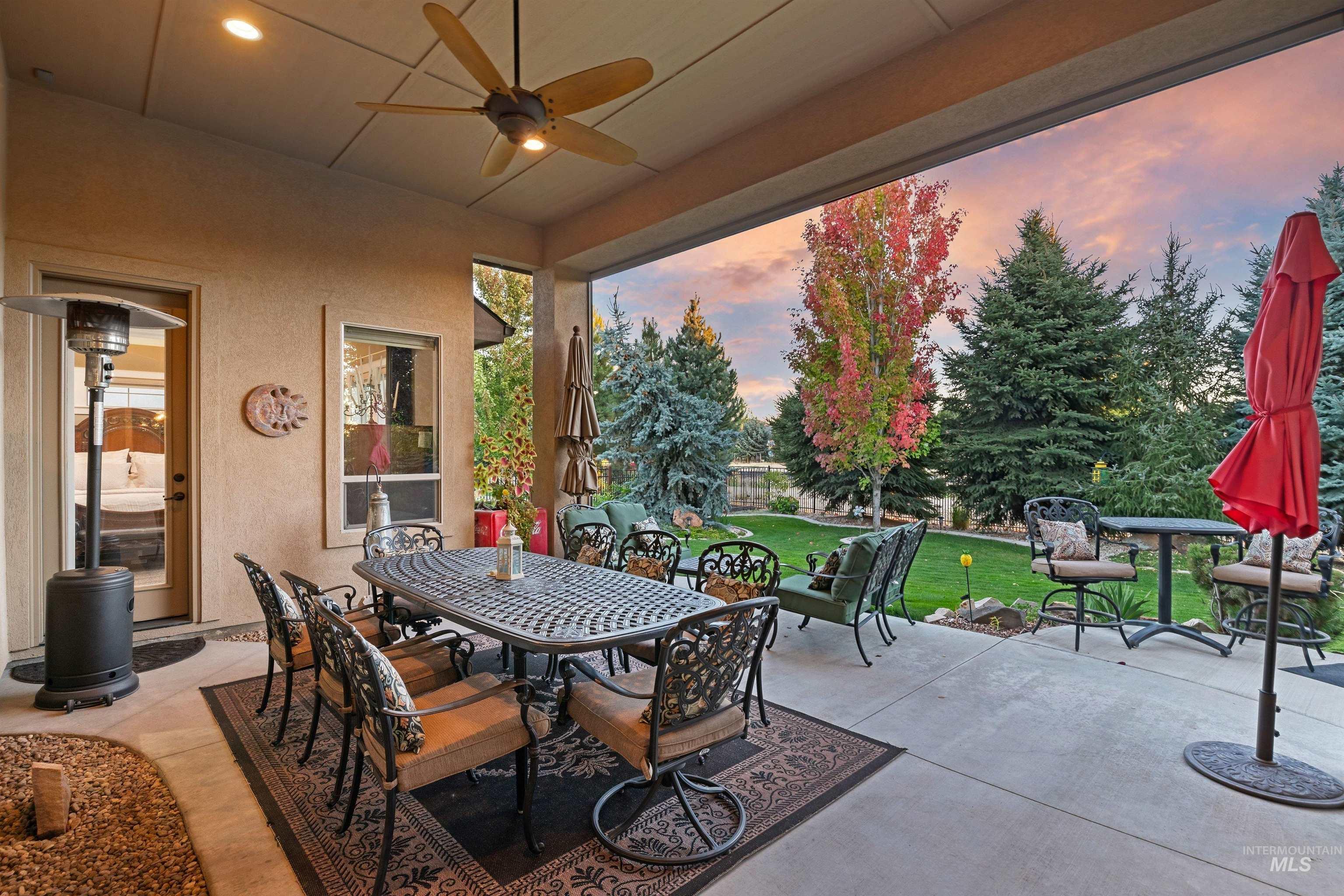 Covered patio with outdoor dining set and seating overlooking a landscaped lawn and autumn trees.