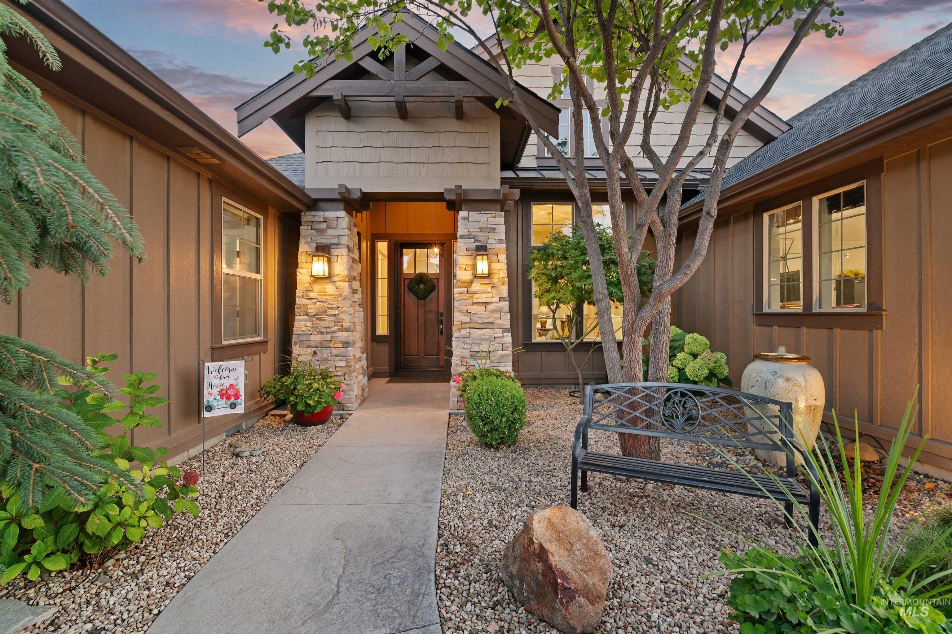 Home entrance with stone columns, a covered porch, and a landscaped gravel courtyard at dusk.