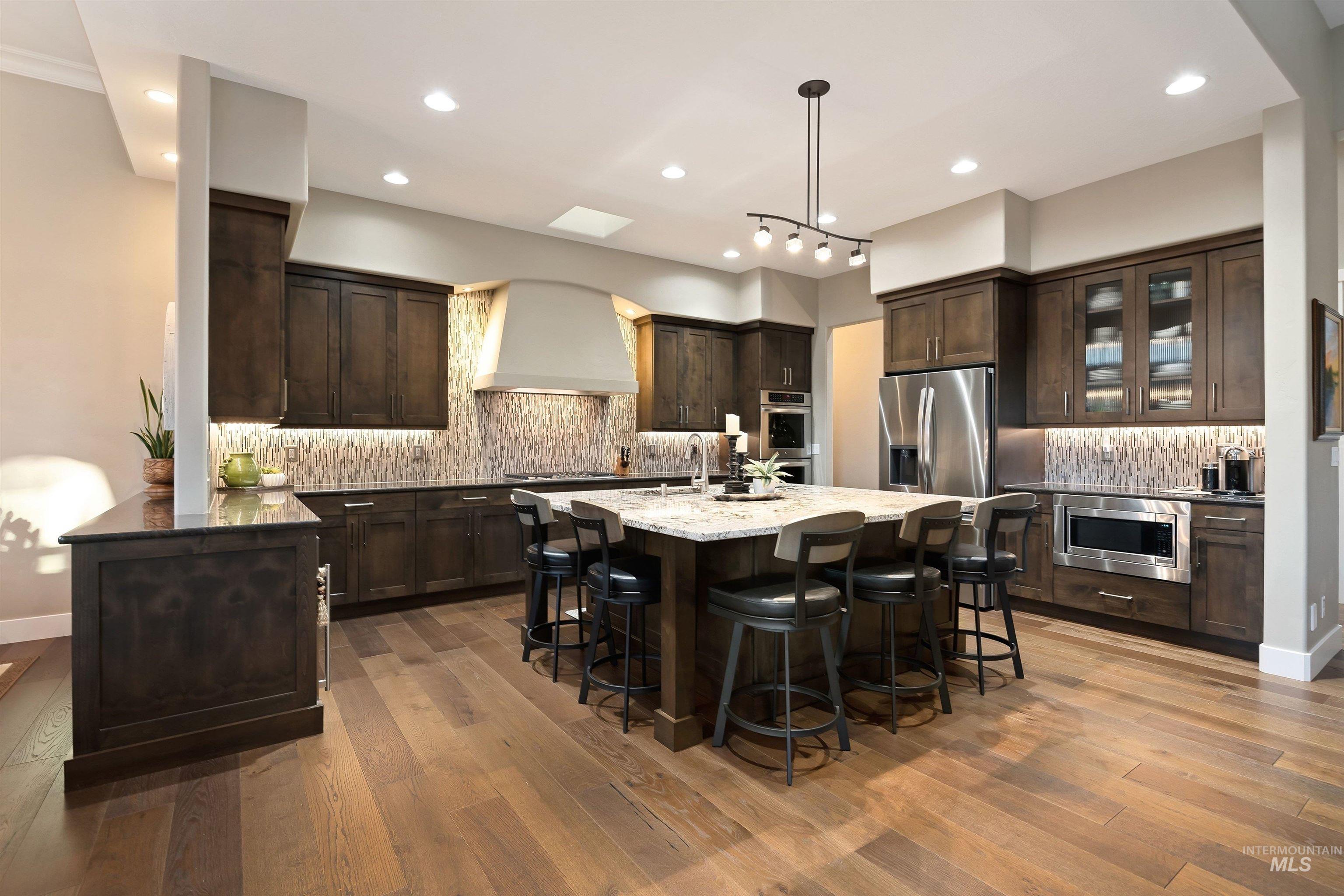 Kitchen with dark wood cabinets, a large stone island, bar seating, and stainless steel appliances.