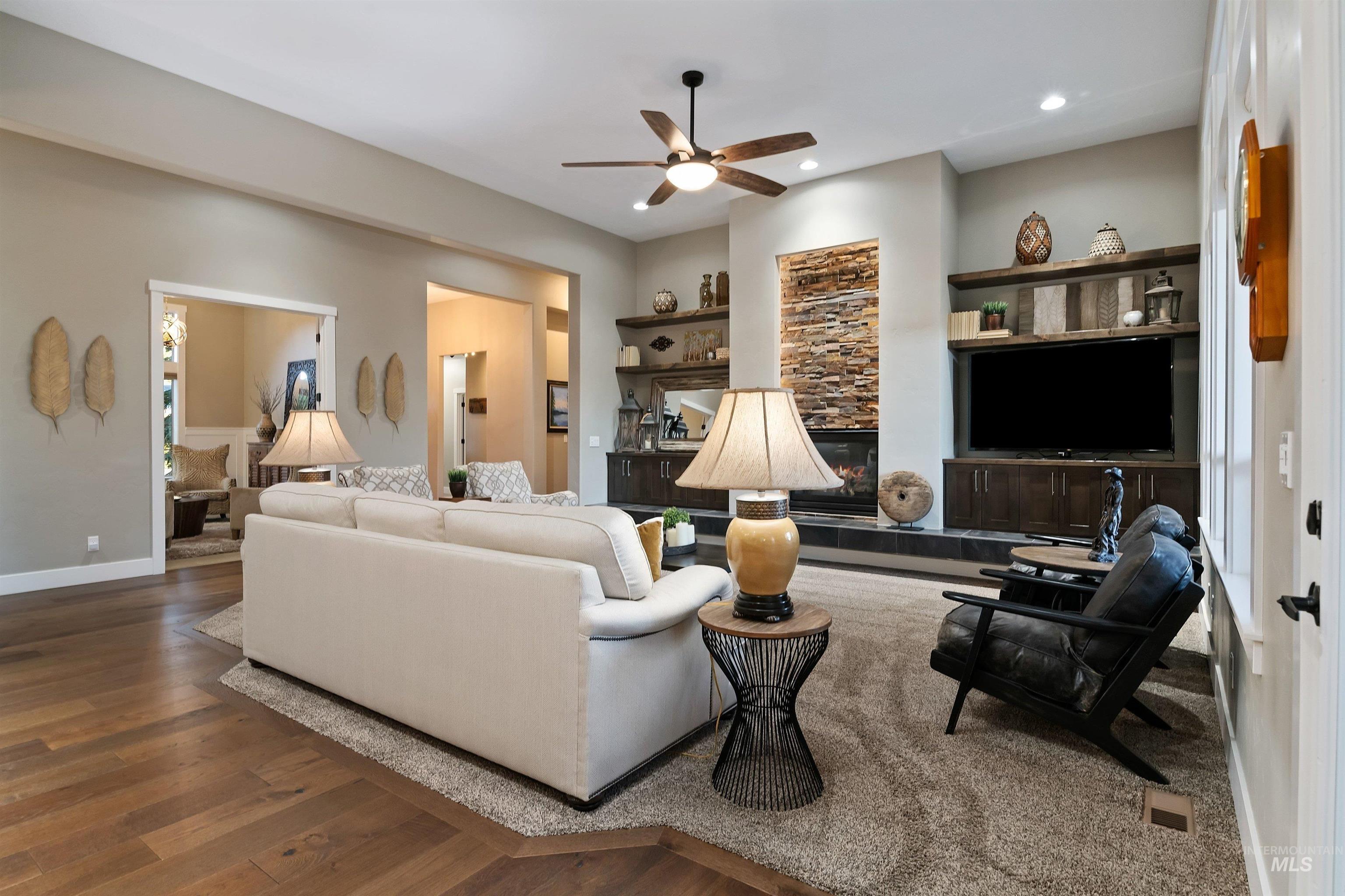 Living room with a white sectional, stone fireplace, built-in TV cabinetry, and black leather chairs.