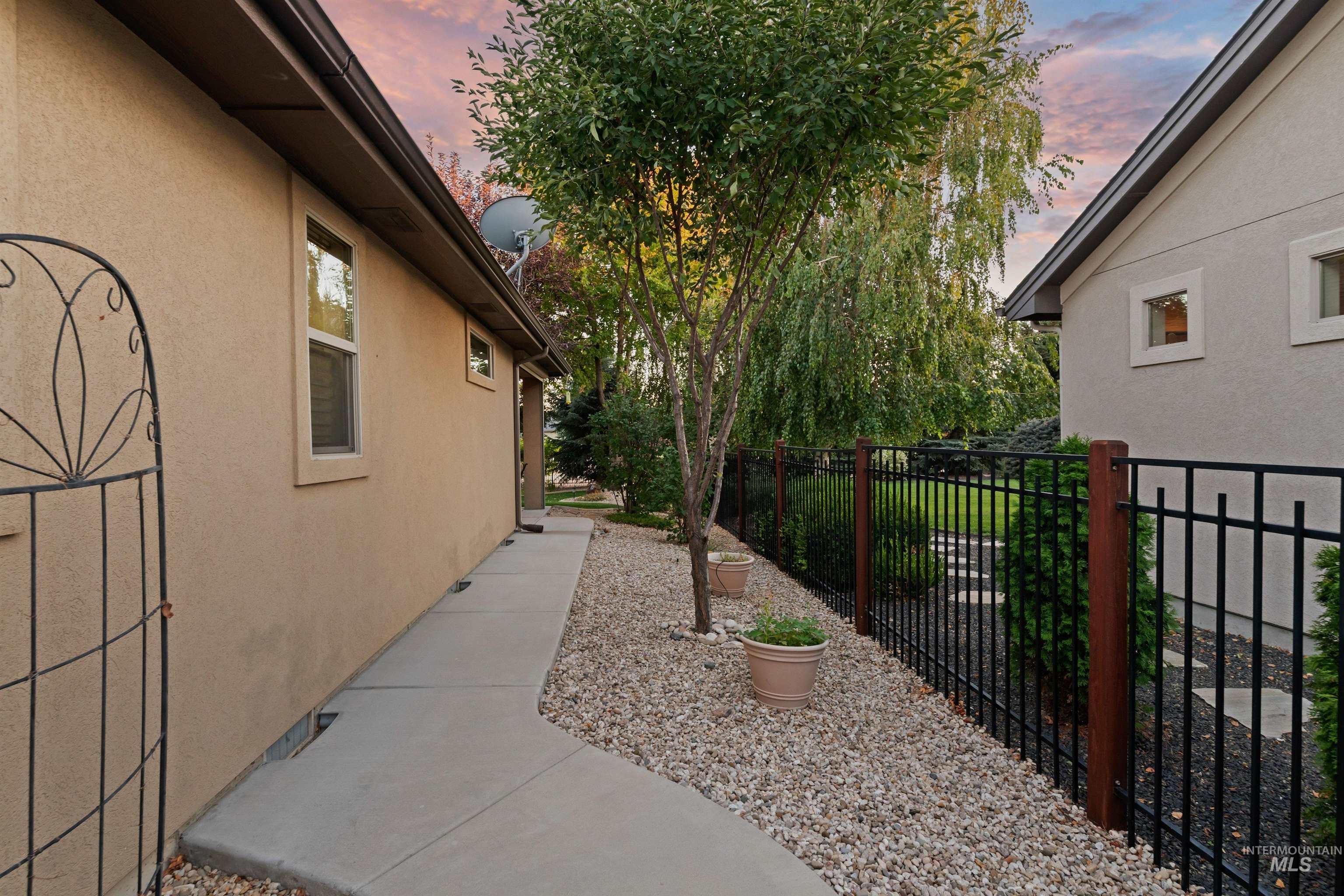 Side yard with a curved walkway, gravel landscaping, mature trees, and a black metal fence.