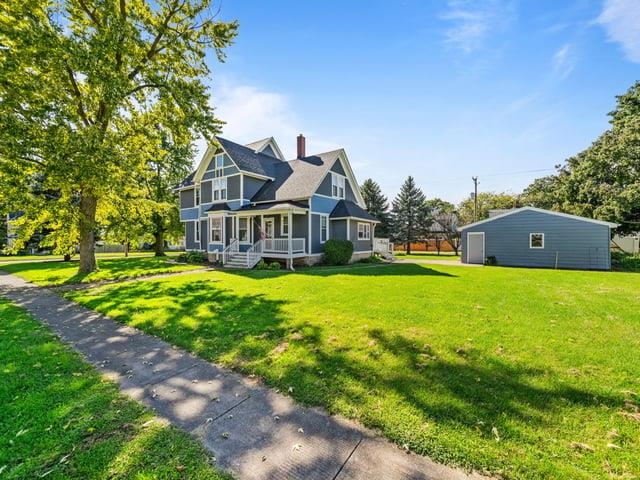 Blue two-story house with a covered porch, detached garage, and mature trees beside the lawn.