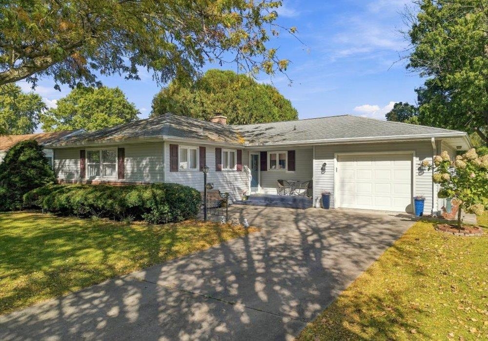 Single-story ranch home with an attached garage, paved driveway, and mature trees.
