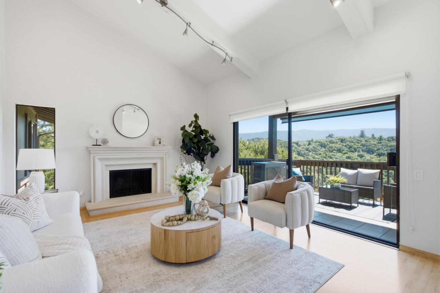 Staged living room with a white fireplace and sliding doors opening to a deck with wooded hill views.