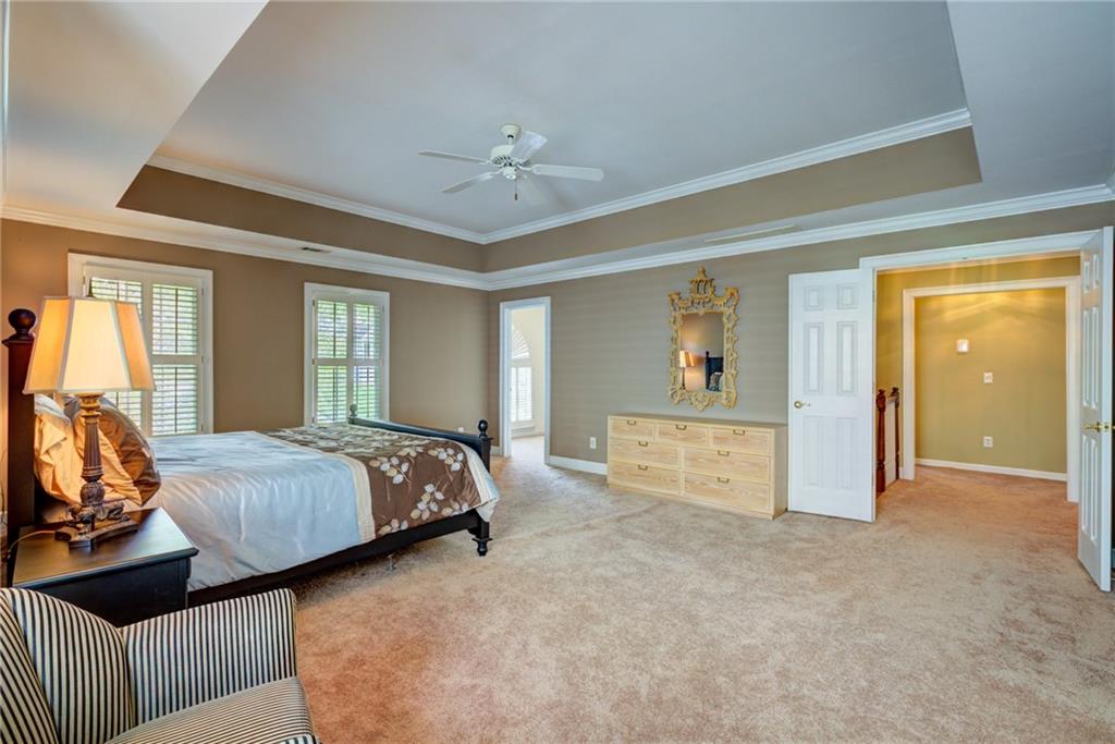 Bedroom with a black four-poster bed, shuttered windows, and a tray ceiling with a ceiling fan.
