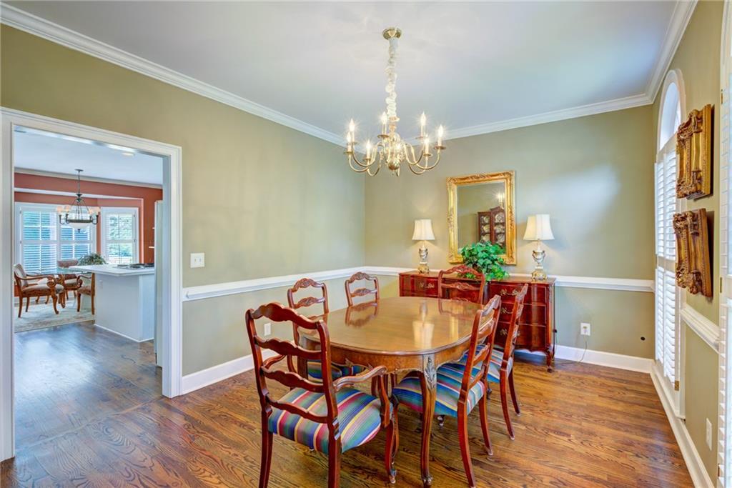 Dining room with a polished wood table, colorful chairs, and chandelier beside an open doorway to the kitchen.