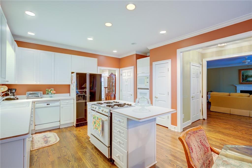 Kitchen with white cabinetry, a central cooktop island, orange walls, and wood flooring.