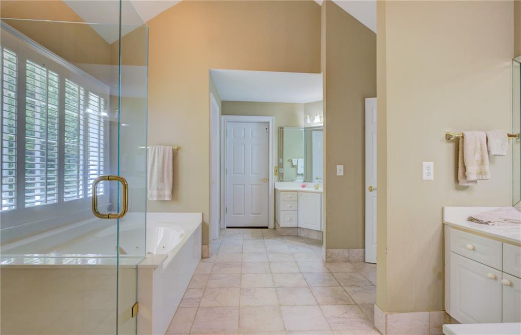 Spacious bathroom with a soaking tub, glass shower enclosure, and shuttered windows.