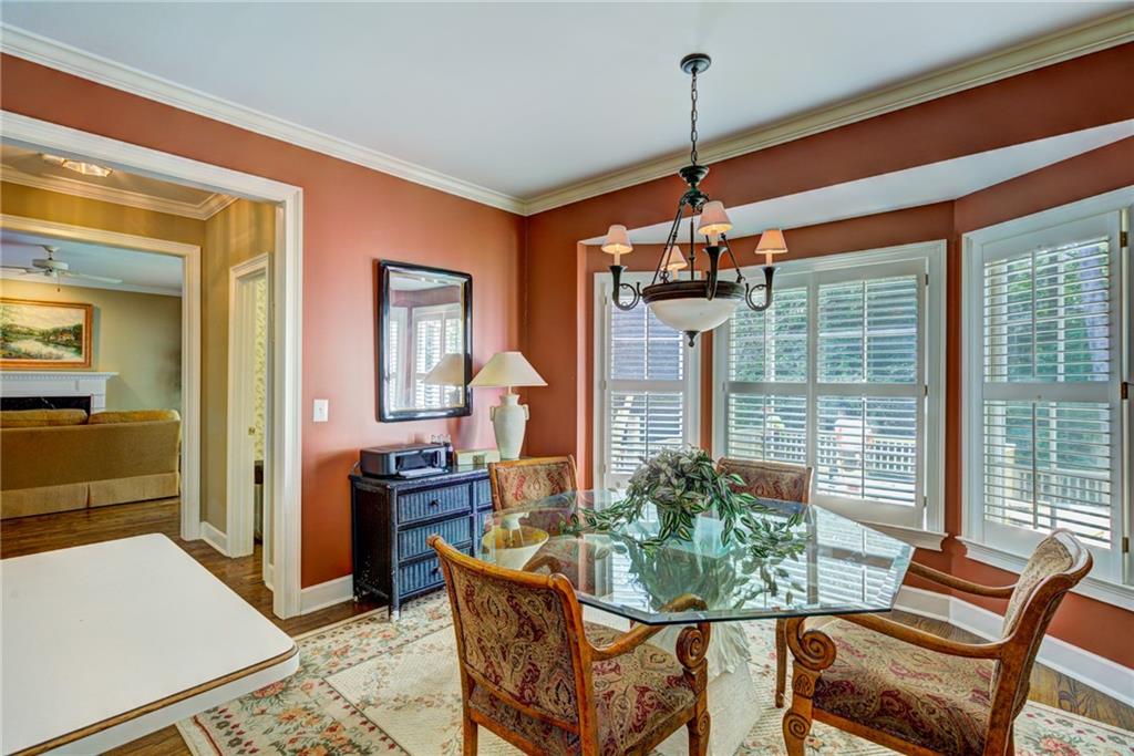 Dining room with a glass-top table, patterned chairs, and large shuttered windows.