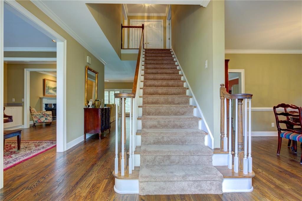 Foyer with a carpeted staircase, white railings, and hardwood floors.