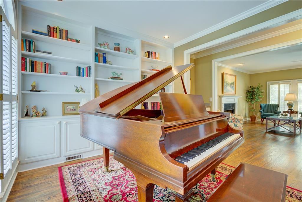 Music room with a polished grand piano, built-in bookshelves, and an adjoining sitting area.