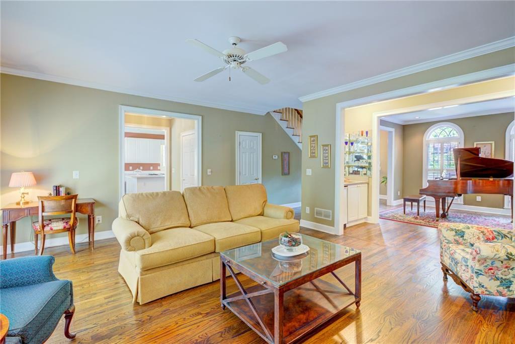 Living room with a tan sectional, hardwood floors, and a grand piano in the adjacent room.