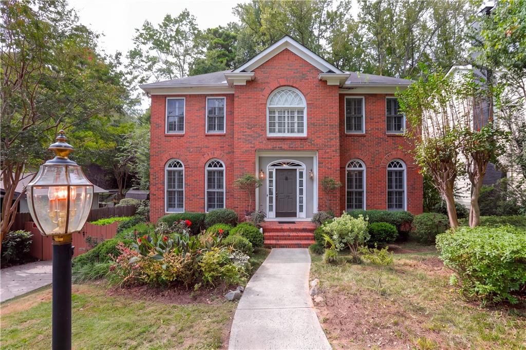 Two-story red brick house with arched windows, a landscaped front garden, and a curved walkway.