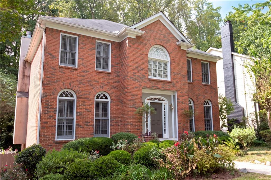 Two-story red-brick house with arched windows and landscaped front garden.