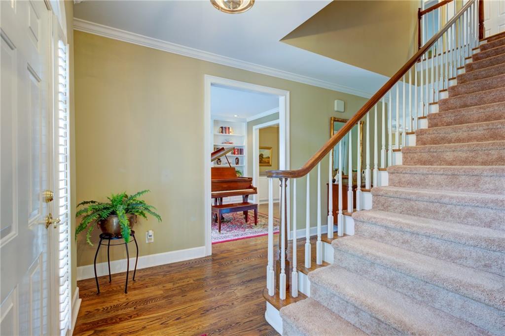Foyer with a carpeted staircase, hardwood floors, and a piano visible through the doorway.