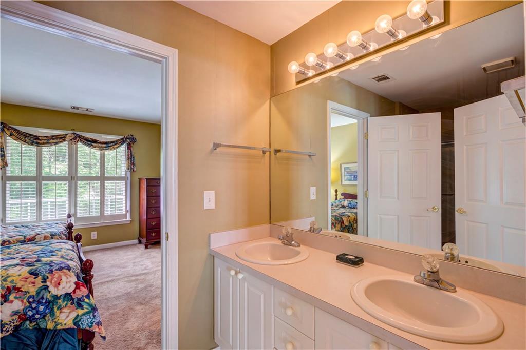 Bathroom with a double-sink vanity and large mirror, opening to a bedroom with floral bedding.