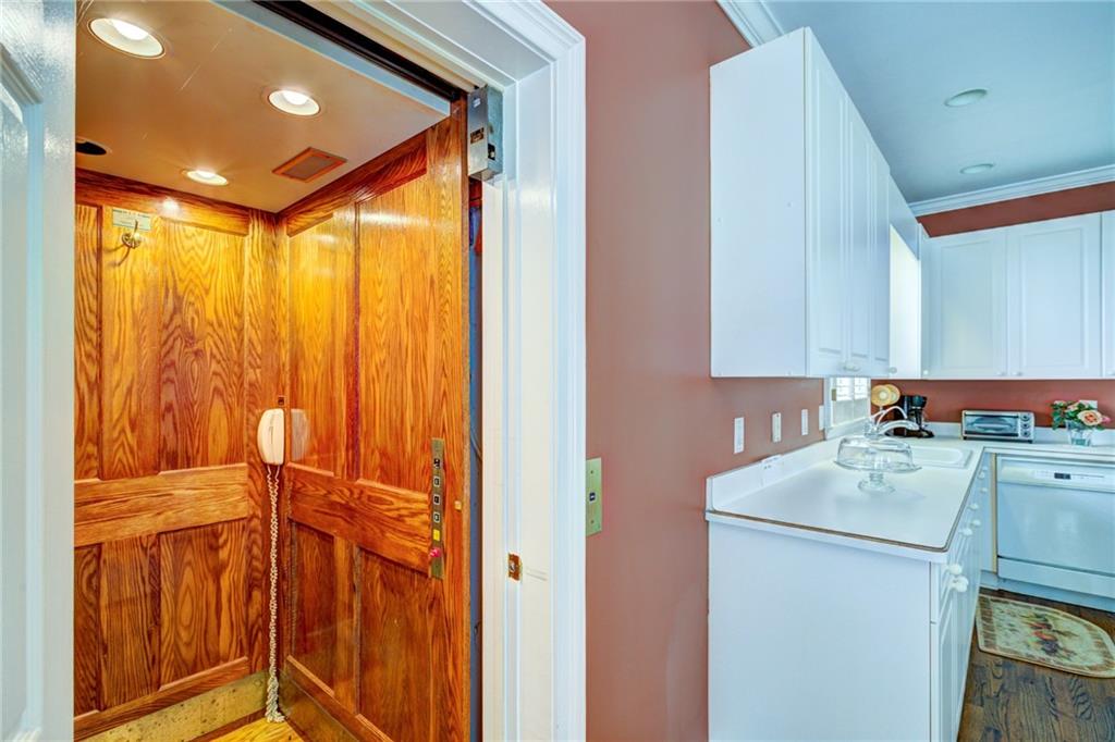 Wood-paneled elevator beside a white kitchen with cabinets and wood flooring.