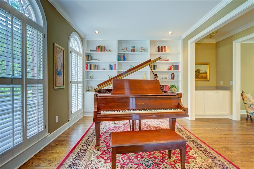Music room with a grand piano, built-in bookshelves, and tall arched windows with plantation shutters.