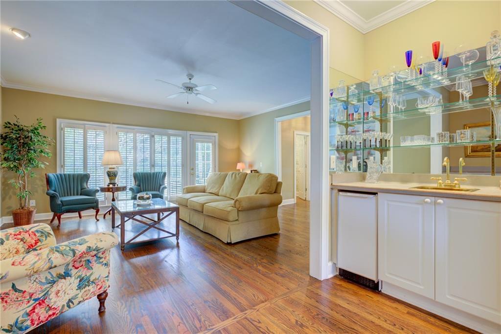 Living room with shuttered windows, hardwood floors, and an adjoining glass-shelf wet bar.