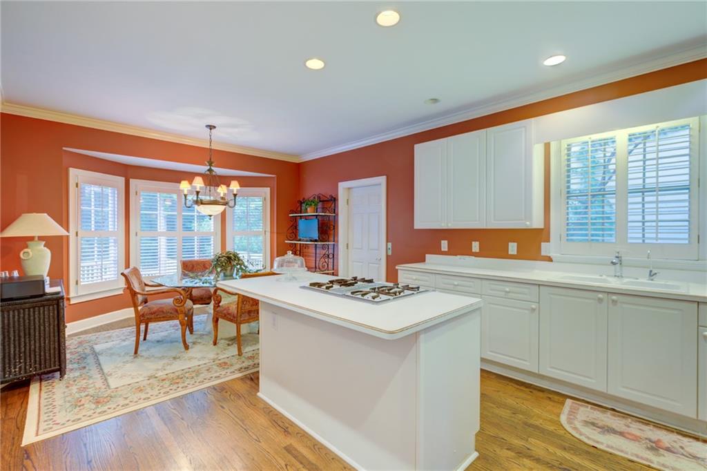 Kitchen with a large white island, gas cooktop, and dining nook by shuttered windows.