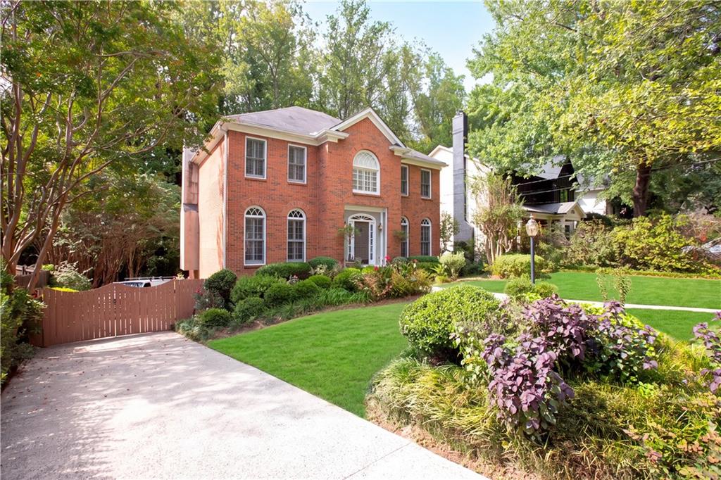 Two-story red-brick house with arched windows, a gated driveway, and landscaped front garden.