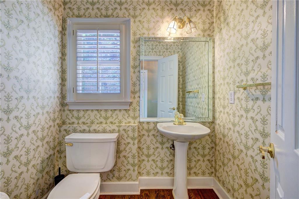 Bathroom with ornate wallpaper, a pedestal sink, and a shuttered window.