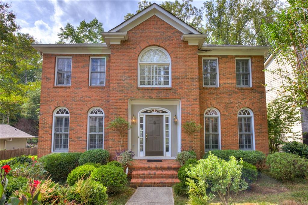 Two-story red brick house with arched windows, a recessed entrance, and landscaped front garden.