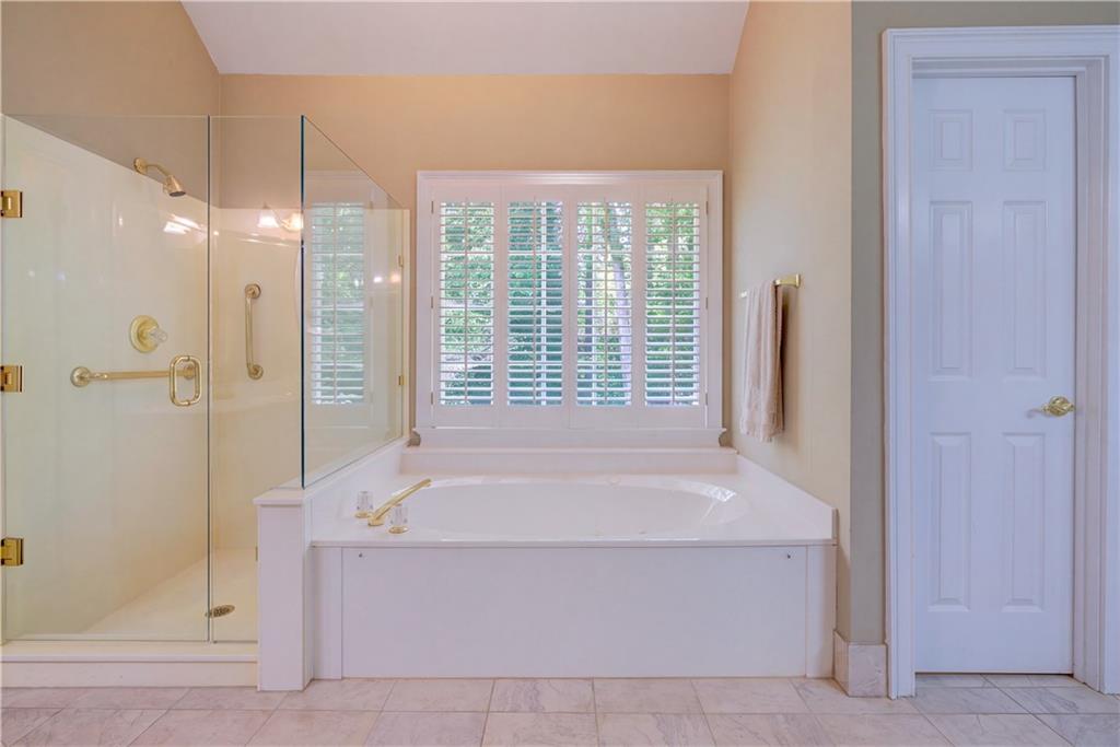 Bathroom with a built-in soaking tub beneath shuttered windows and an adjacent glass shower.