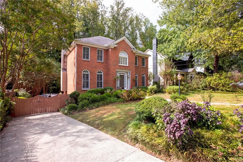 Two-story red brick house with arched windows, landscaped gardens, and a curved driveway.