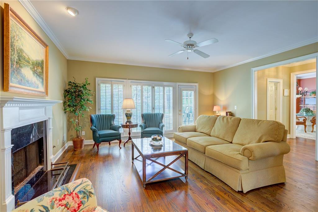 Living room with a white fireplace, hardwood floors, and a tan sofa beside shuttered windows.